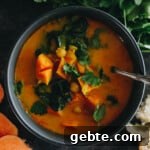curried sweet potato soup with chopped sweet potatoes, chickpeas and swiss chard in a blue bowl.