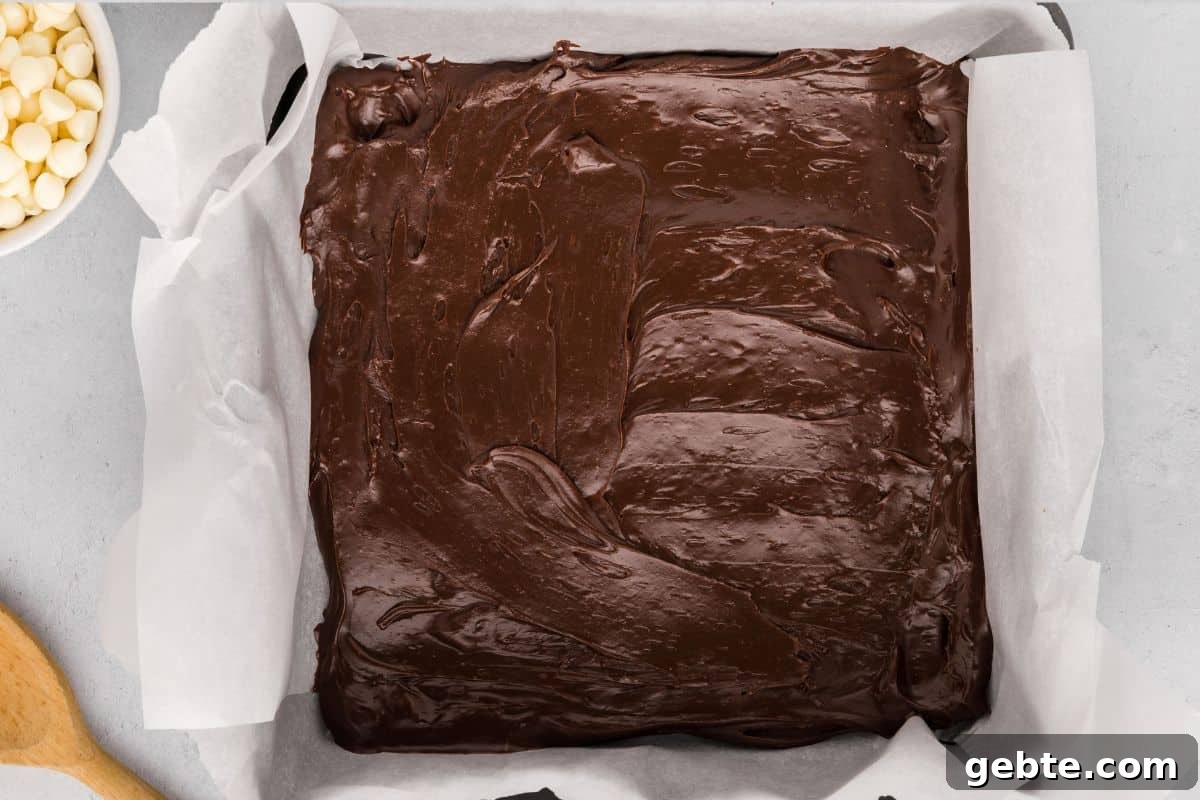 Melted chocolate layer of Christmas fudge spread out in parchment lined baking dish.