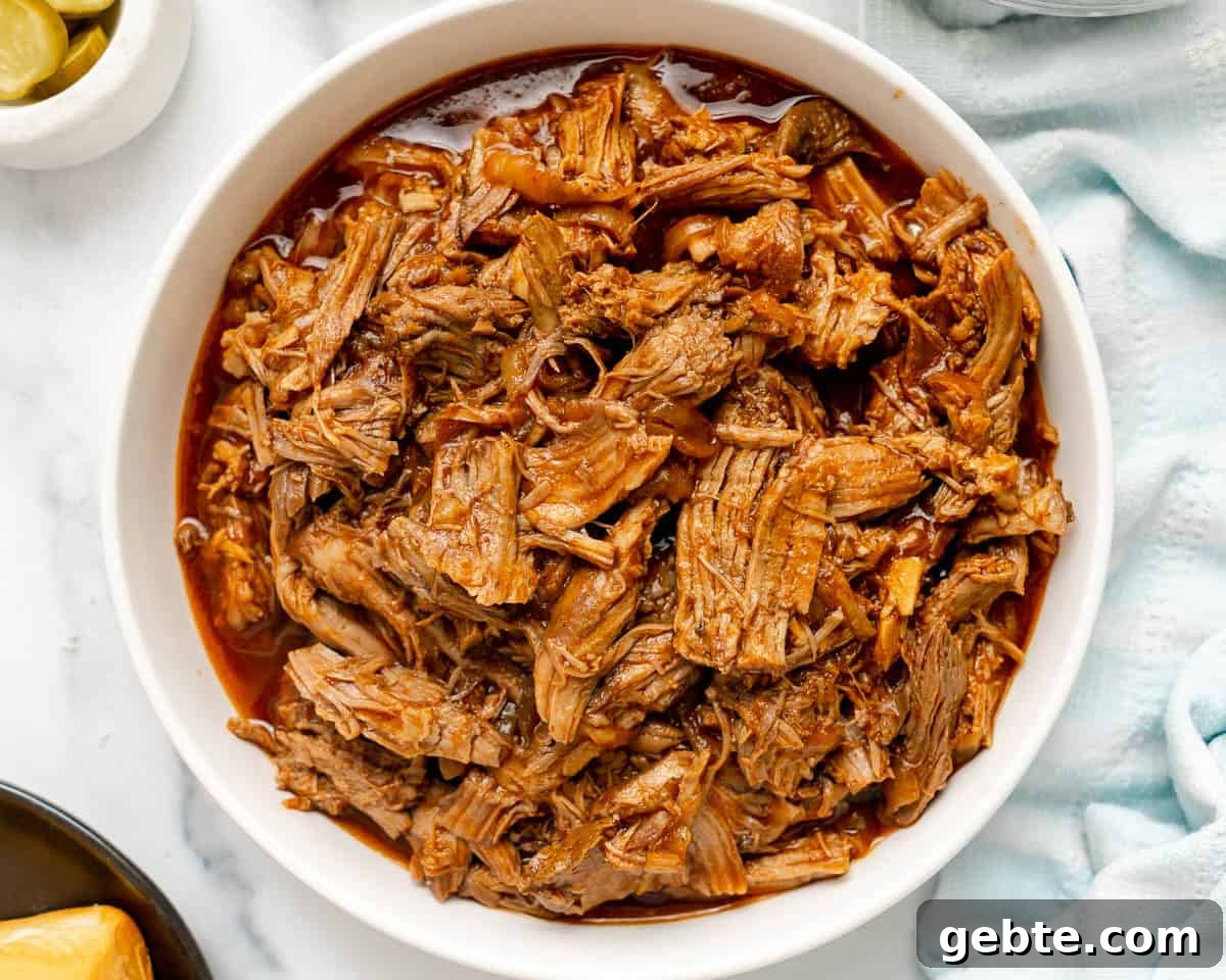 Shredded barbecue pork in a white bowl with visible sauce on a marble surface.