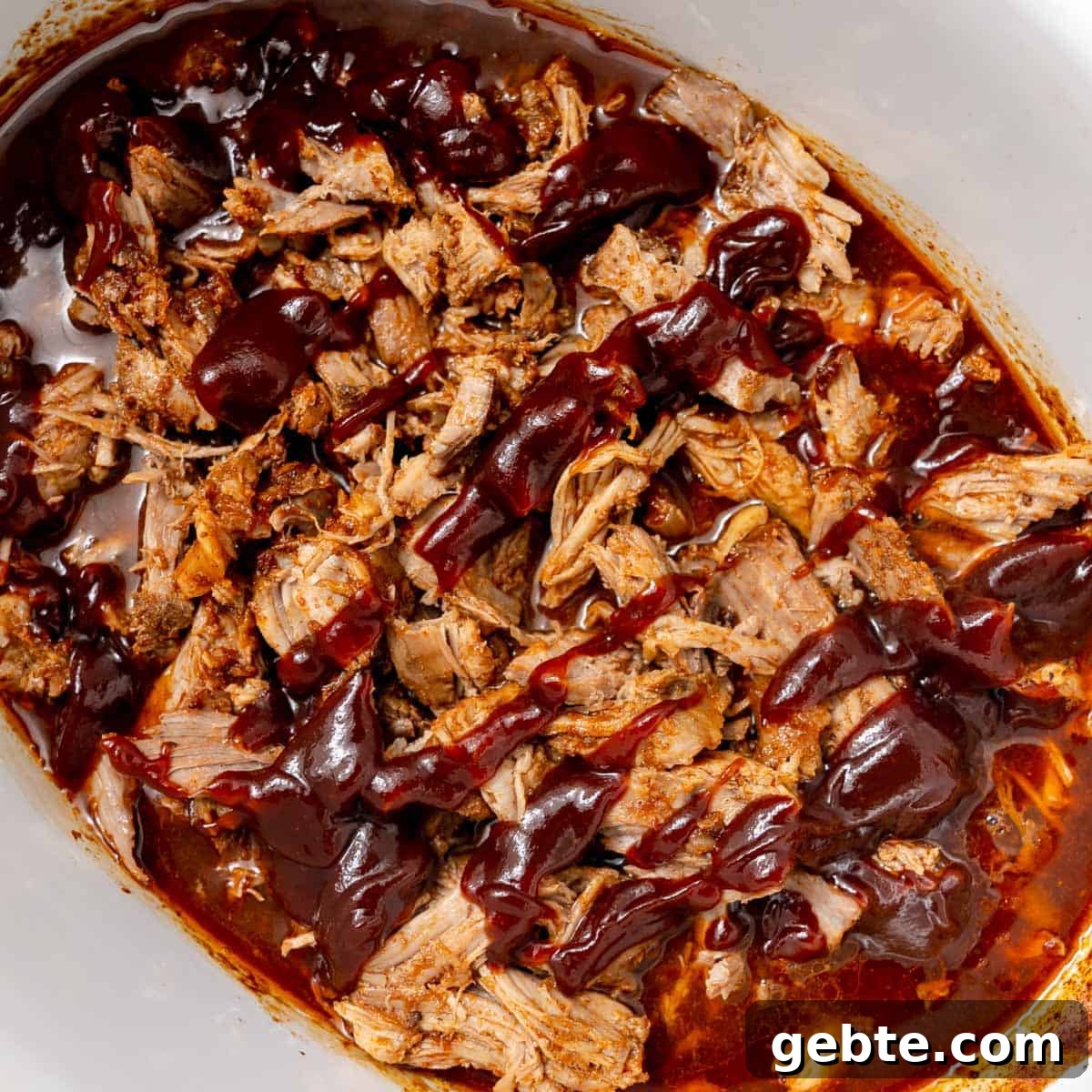 Shredded barbecue pork in sauce, served in a white dish.