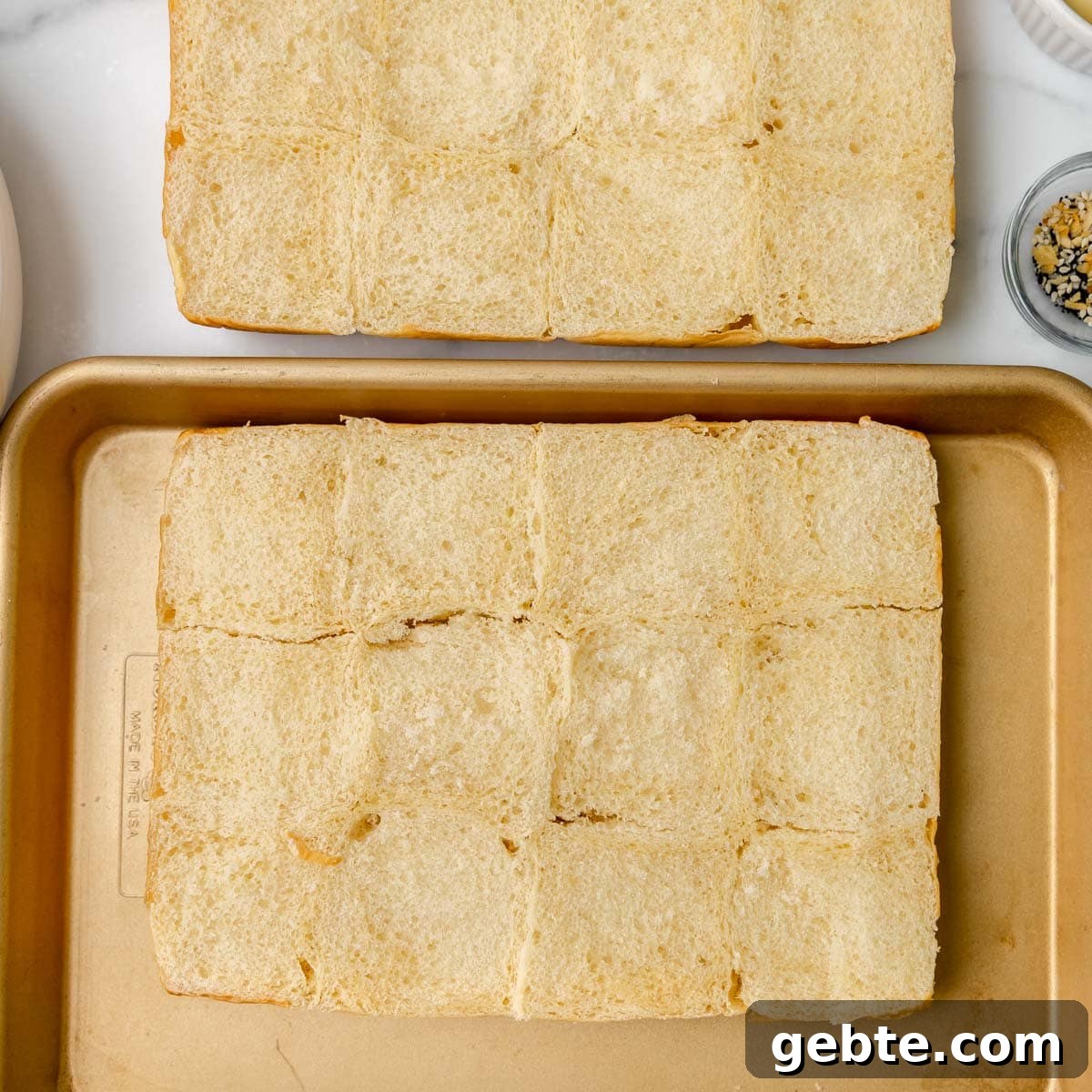 Two rectangular slabs of sliced bread rolls are placed on separate trays, with the top one on a marble surface and the bottom one on a golden baking sheet.
