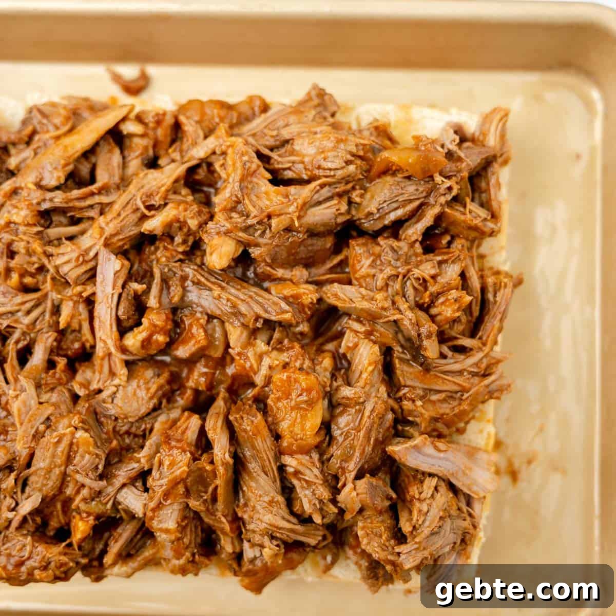 Shredded, pulled pork spread over sliced bread on a baking tray.