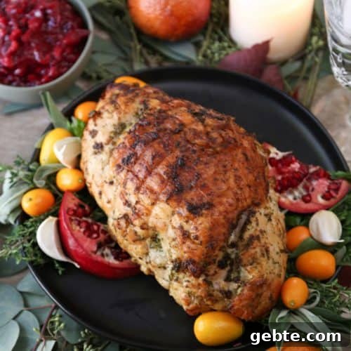 cooked turkey breast on a black platter with pomegranates, herbs, and kumquats for garnish.