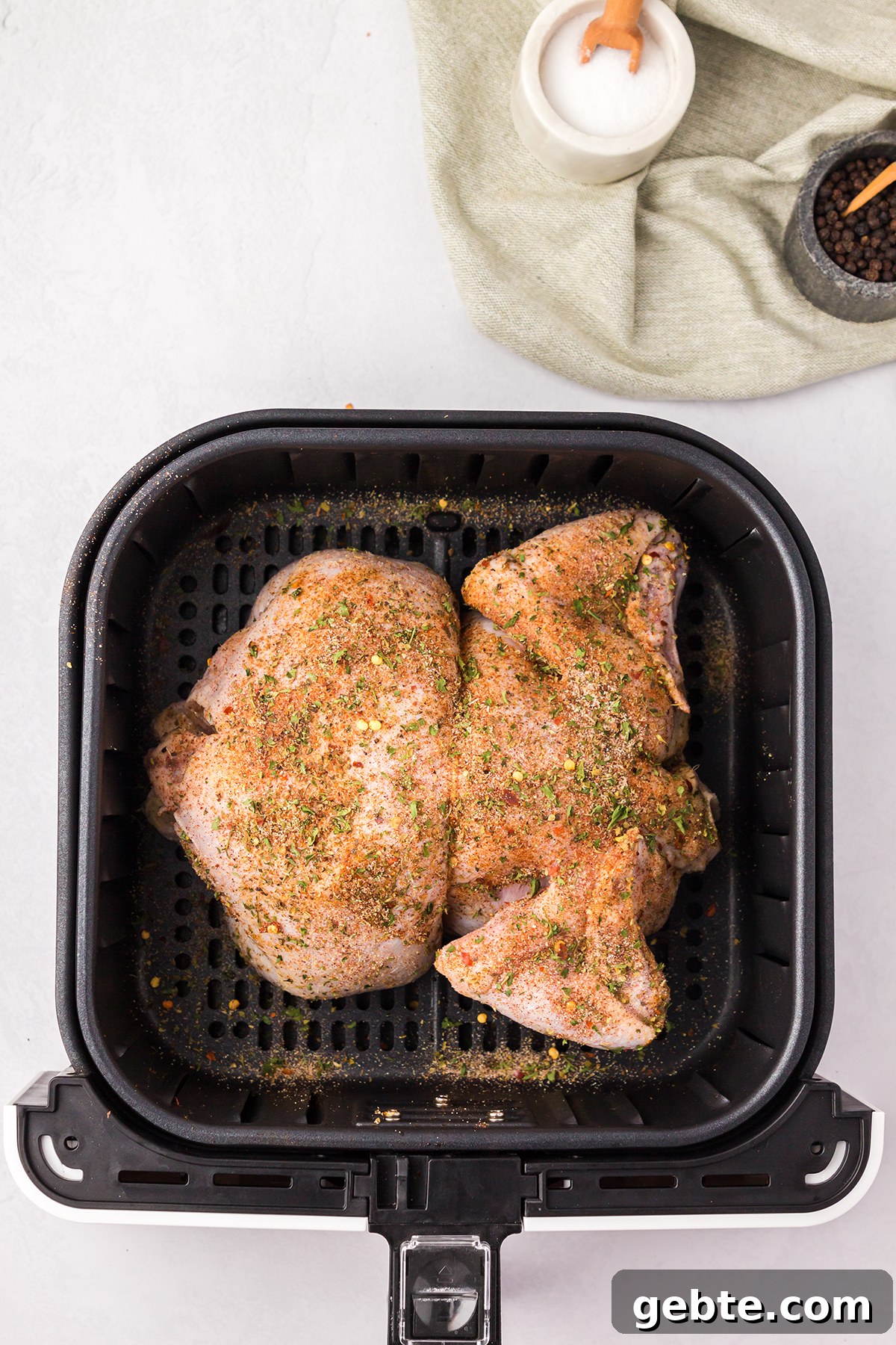 Seasoned whole chicken placed in air fryer basket.