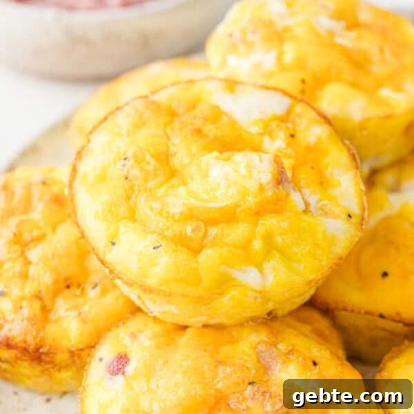 Green Chile Egg White Frittata 8 Close-up of a stack of baked egg muffins with a golden-brown top, featuring visible pieces of ham and cheese.