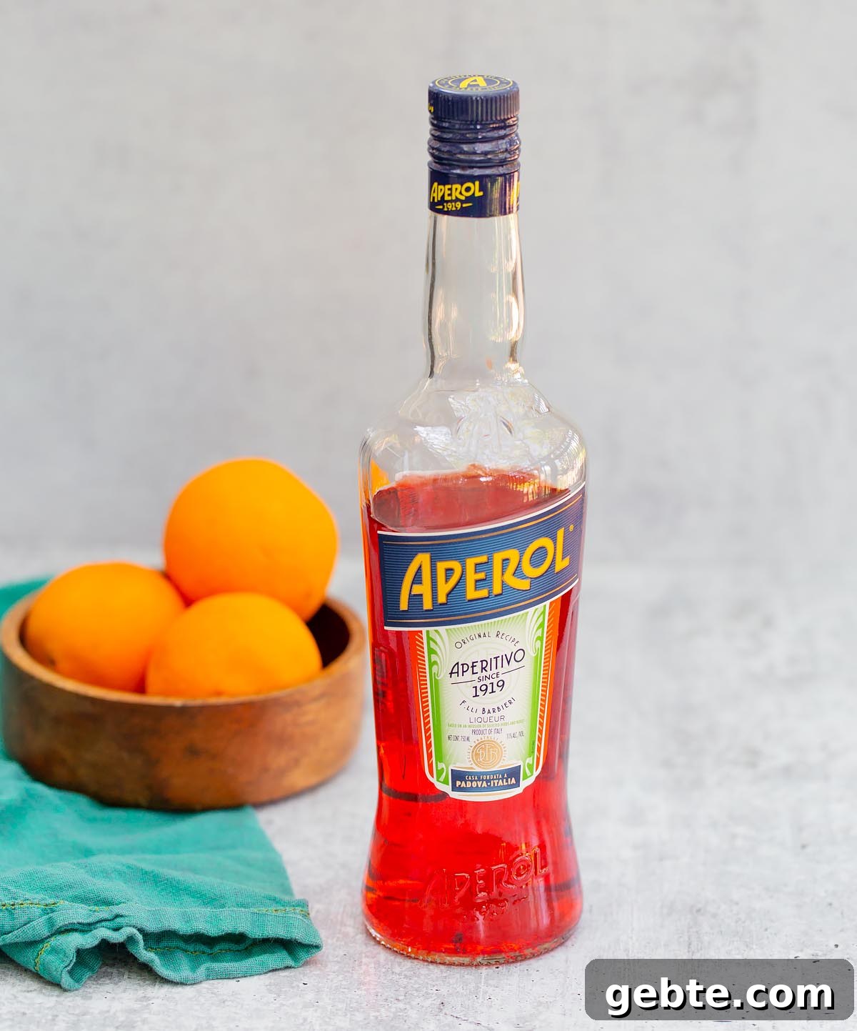 a bottle of aperol with a bowl of oranges in the background