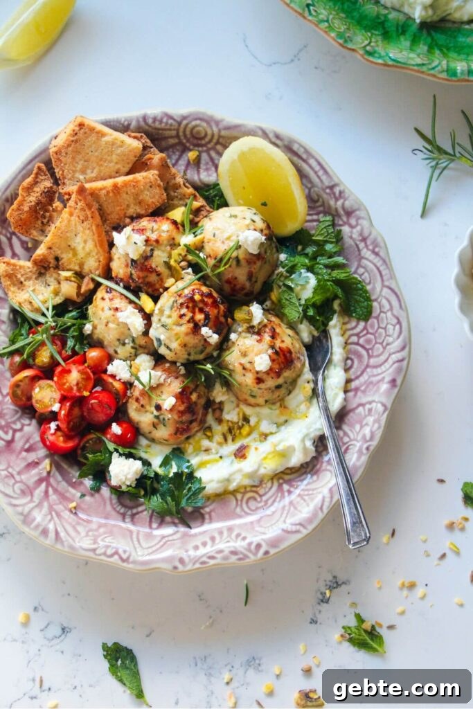 Chicken meatballs, tomatoes, on tzatziki with pita chips on a pink plate.
