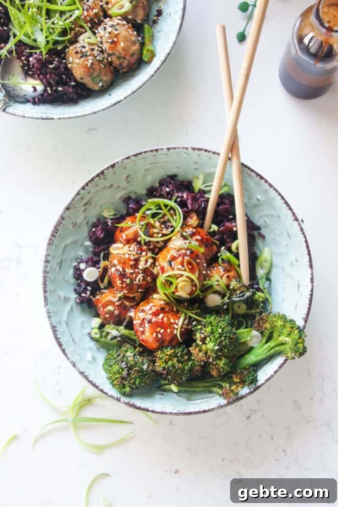 Glazed Asian chicken meatballs with rice and broccoli in a small blue bowl.