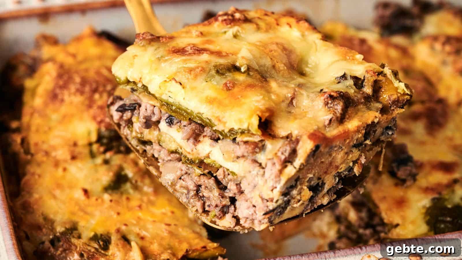 A slice of lasagna with beef, mushrooms, cheese, and vegetables being lifted from a baking dish.