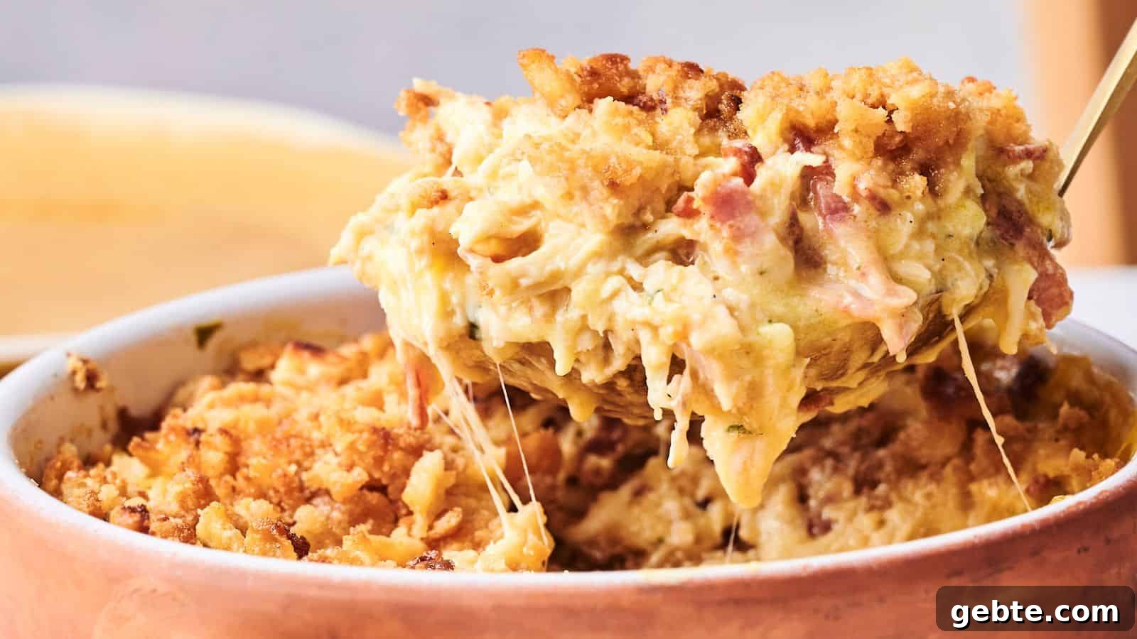 A spoon lifts a serving of baked macaroni and cheese with a golden breadcrumb topping and melted cheese from a casserole dish.