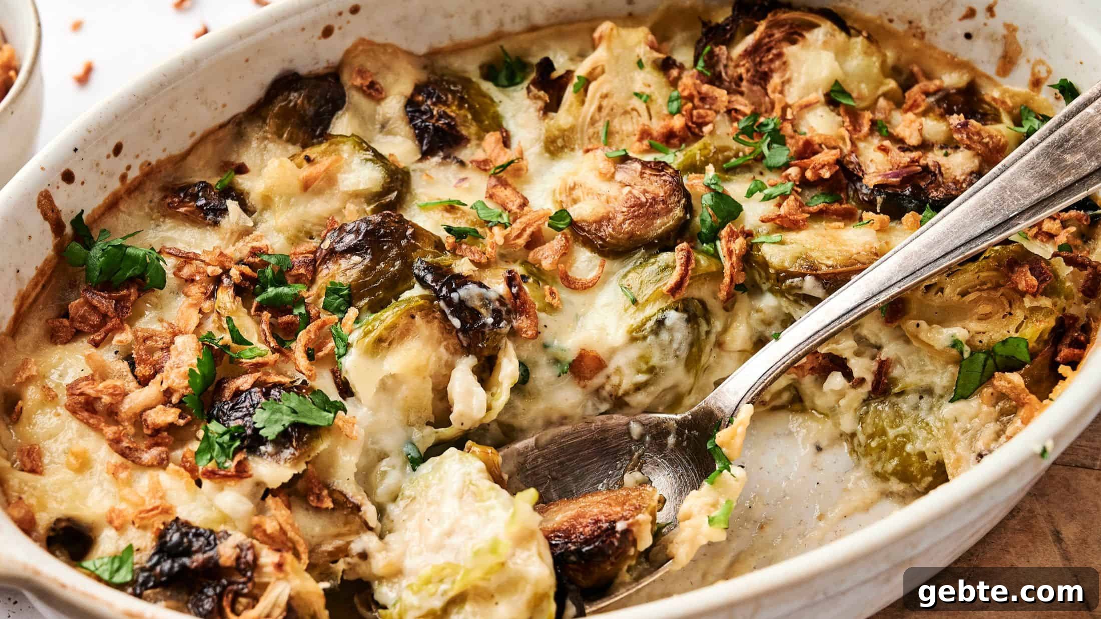 Casserole dish with Brussels sprouts, crispy onions, cheese, and herbs, mixed with a spoon.