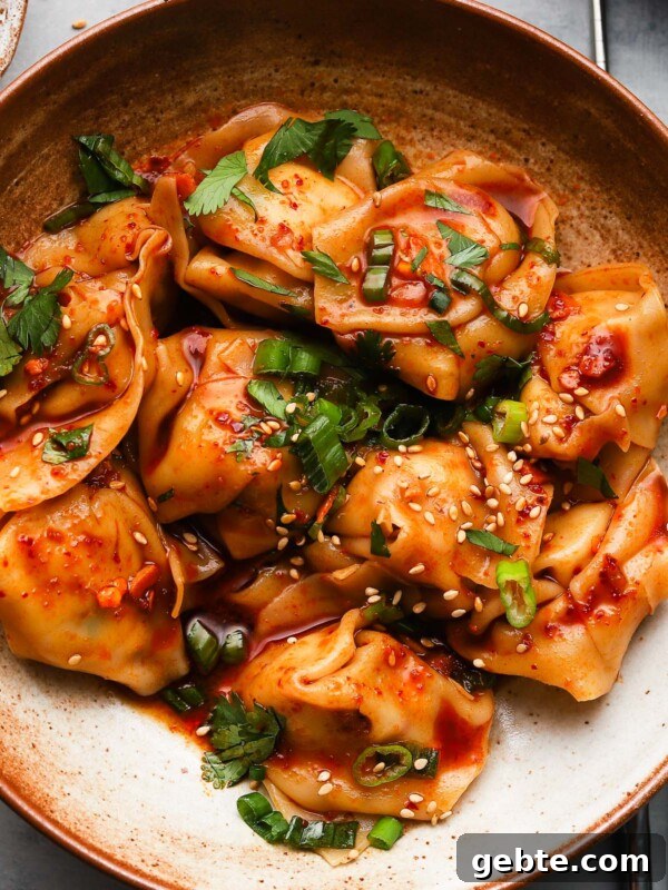 Spicy chicken wontons garnished with sesame seeds and fresh herbs in a ceramic bowl.