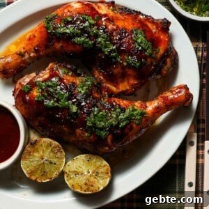 A platter of grilled honey chipotle bbq chicken with grilled limes and cilantro lime gremolata on a plaid tablecloth.