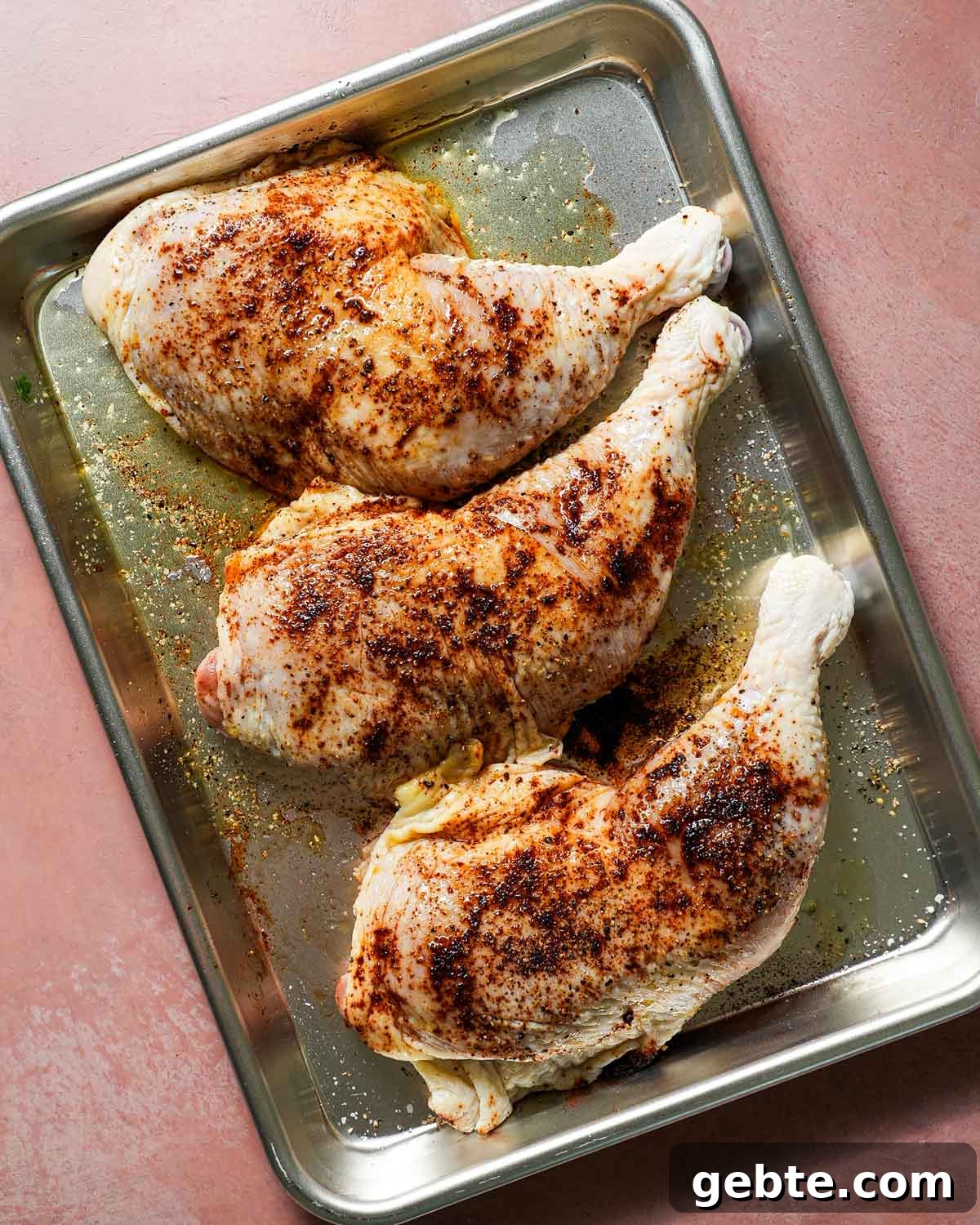 Raw chicken on a baking sheet with chipotle powder, salt, pepper, and olive oil ready to go on the grill.