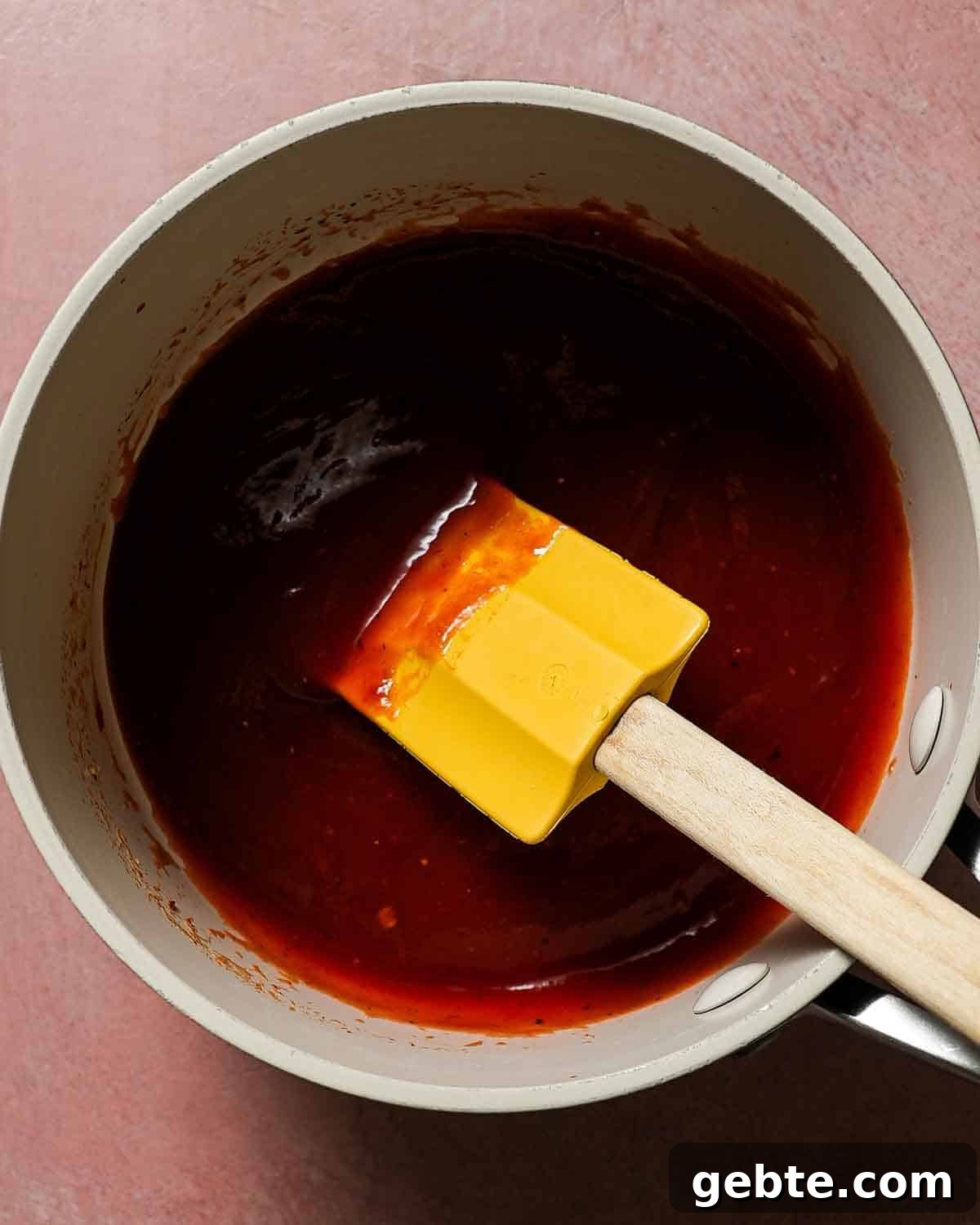 A small pan with chipotle honey bbq sauce with a yellow spatula to stir.