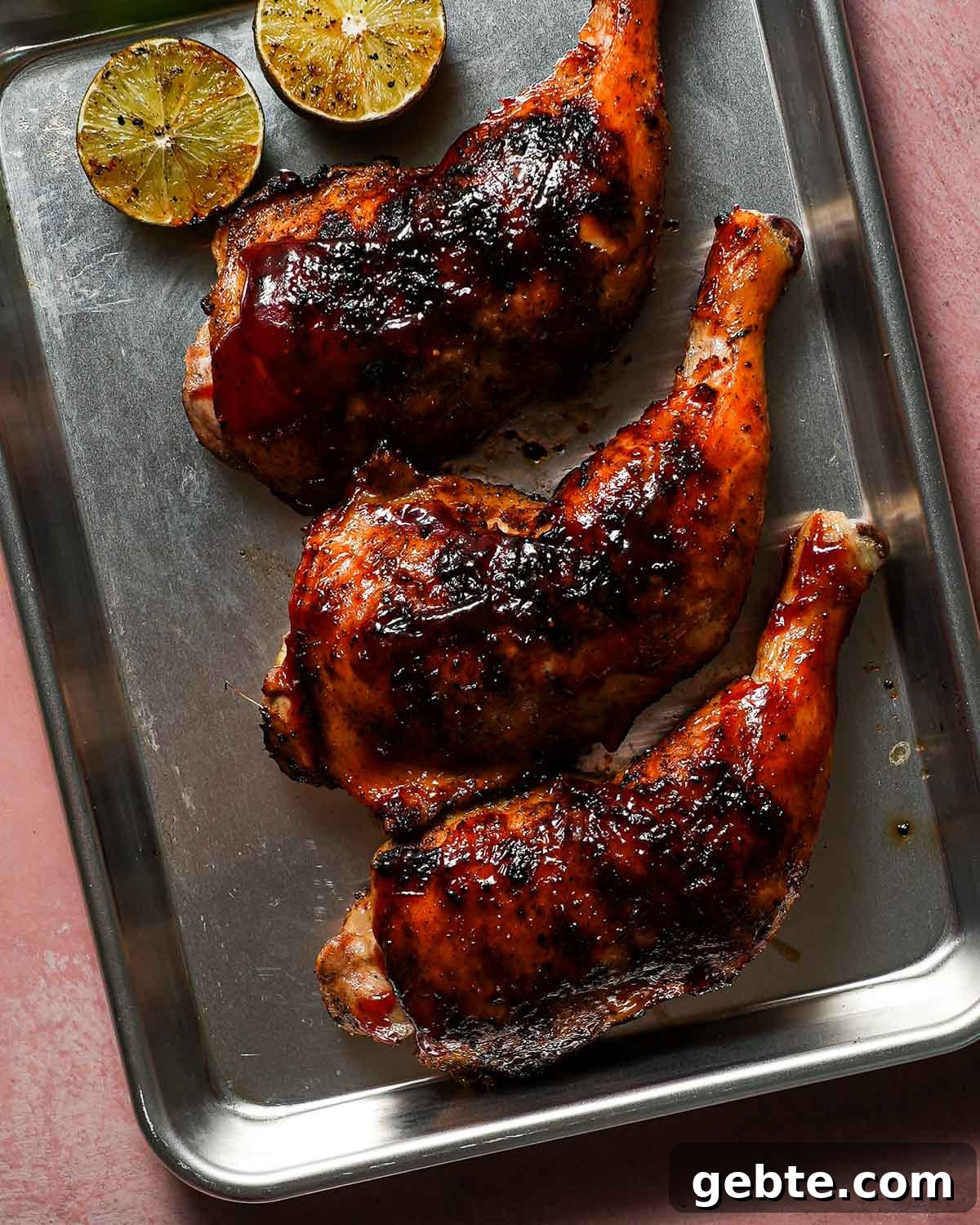 A baking sheet with 3 cooked chicken legs alongside halved grilled limes.