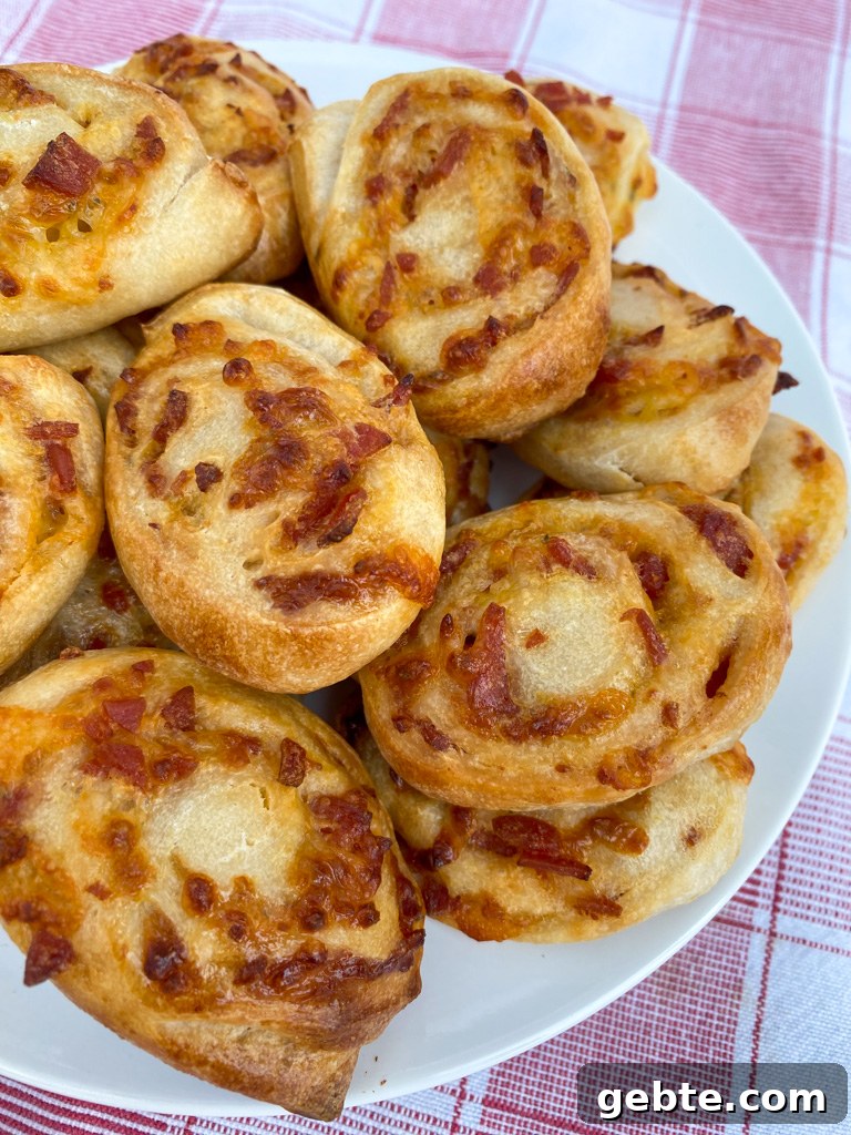 Freshly baked golden brown pepperoni pinwheels on a white plate on a red and white napkin ready to dip in sauce.