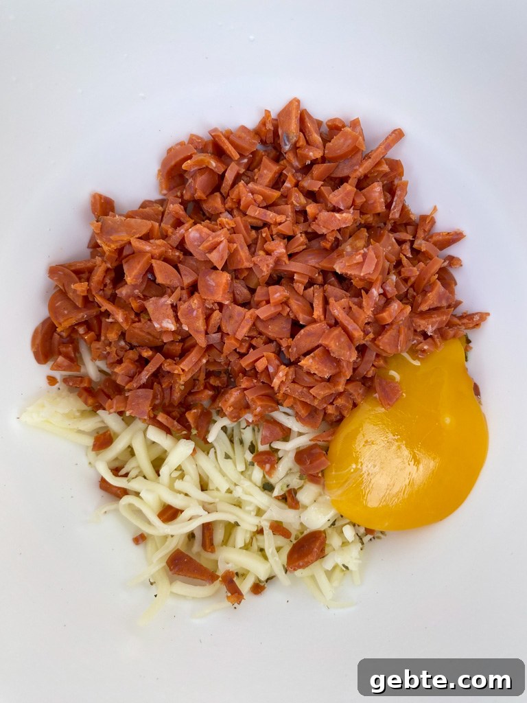 Finely chopped pepperoni poured on top of shredded mozzarella cheese with an egg yolk on the side in a small white mixing bowl.
