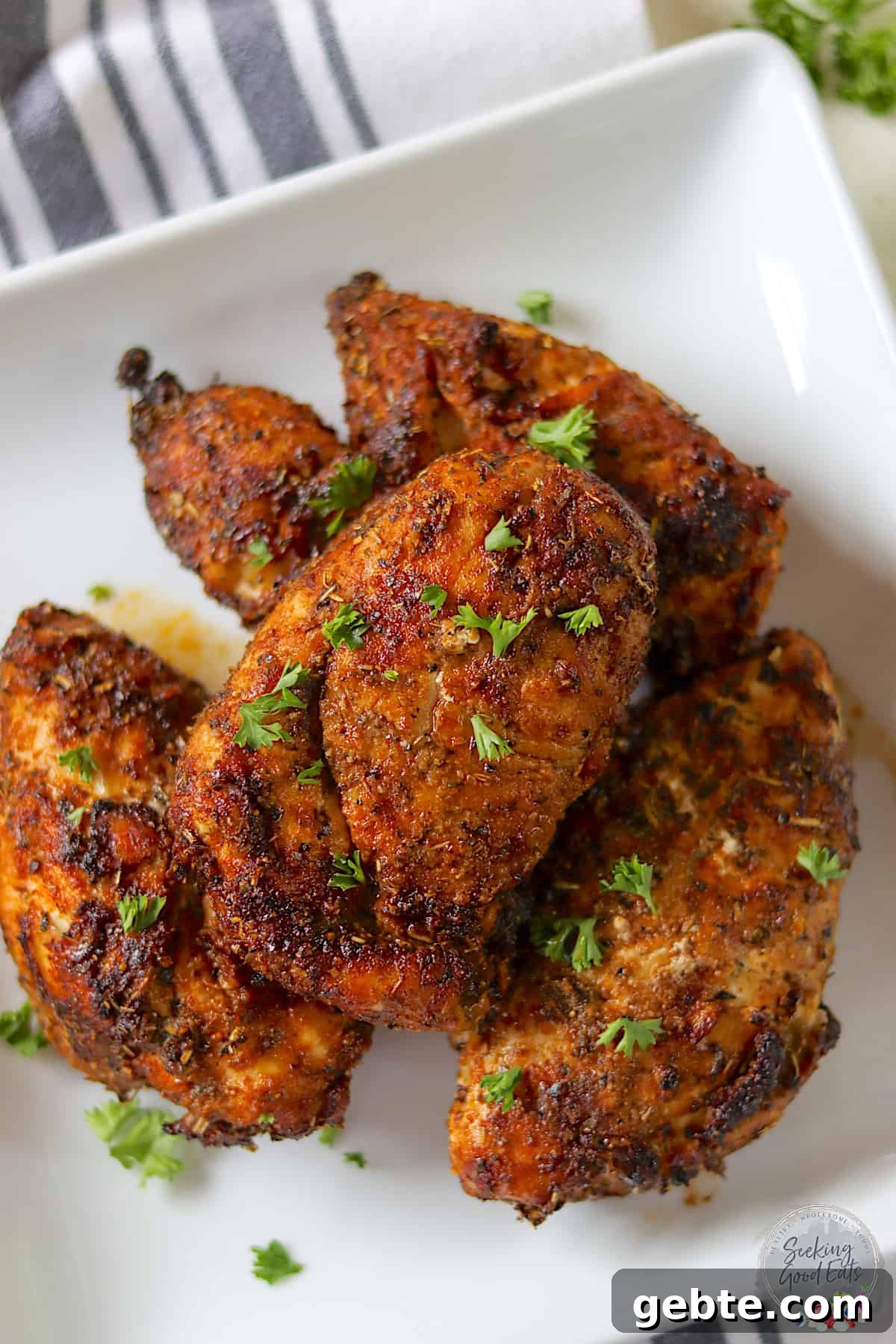 Four air fryer chicken breasts on a square white plate garnished with parsley.
