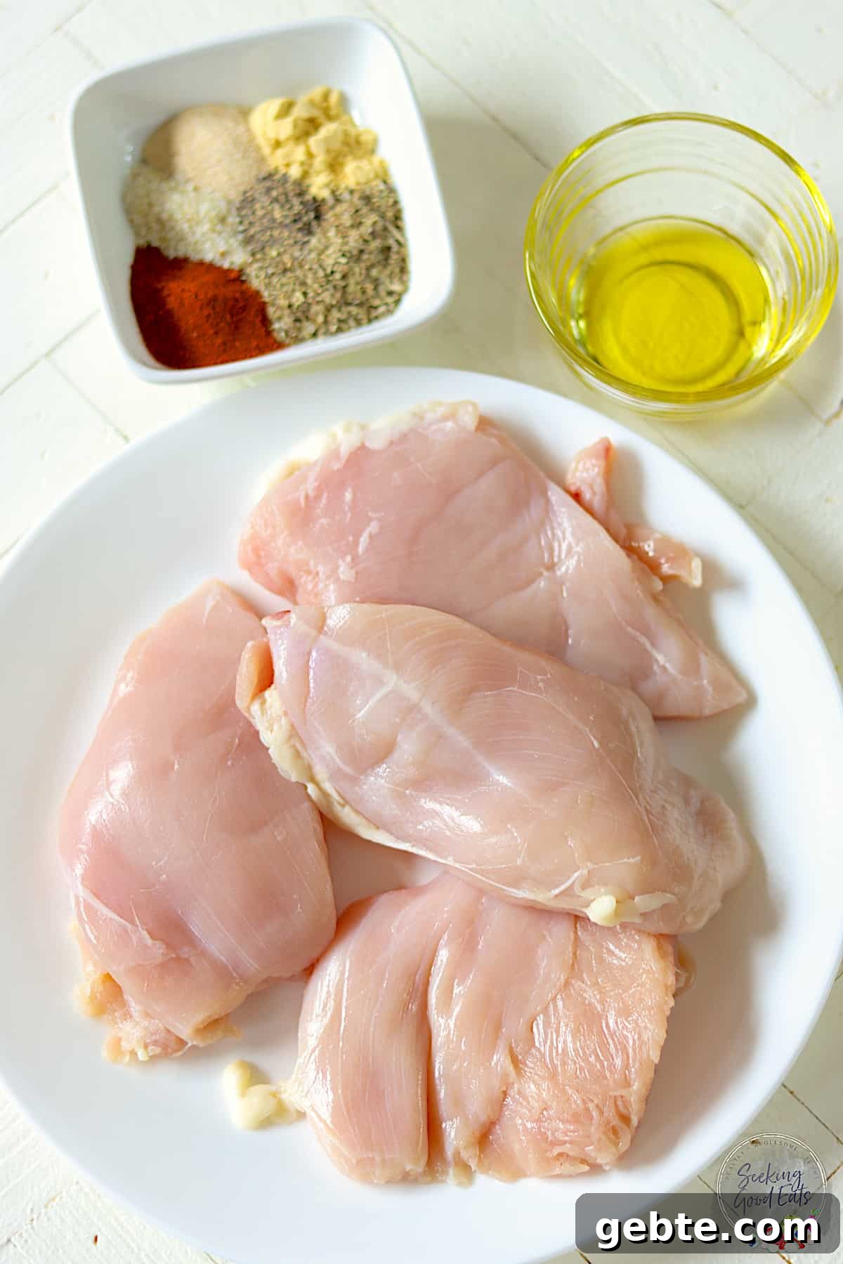 Ingredients needed for making air fryer chicken breasts on a wooden white table.