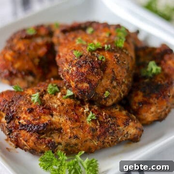 Golden air fried chicken breasts on a white plate garnished with fresh parsley.