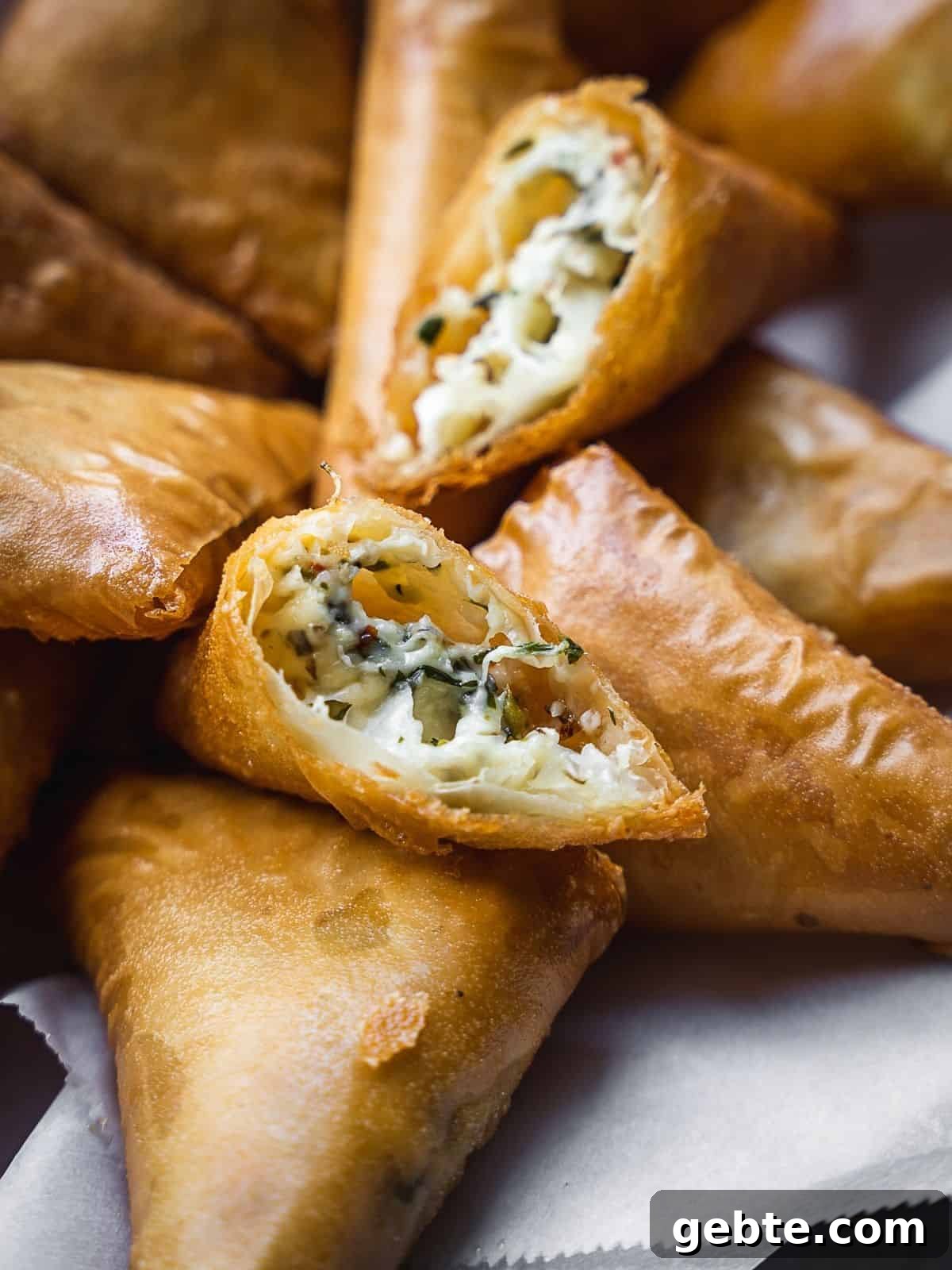 Crispy Cheese Sambousek: Middle Eastern Fried Pastries 7 Deep fried pastries in a bowl with one pastry opened exposing the cheesy filling.