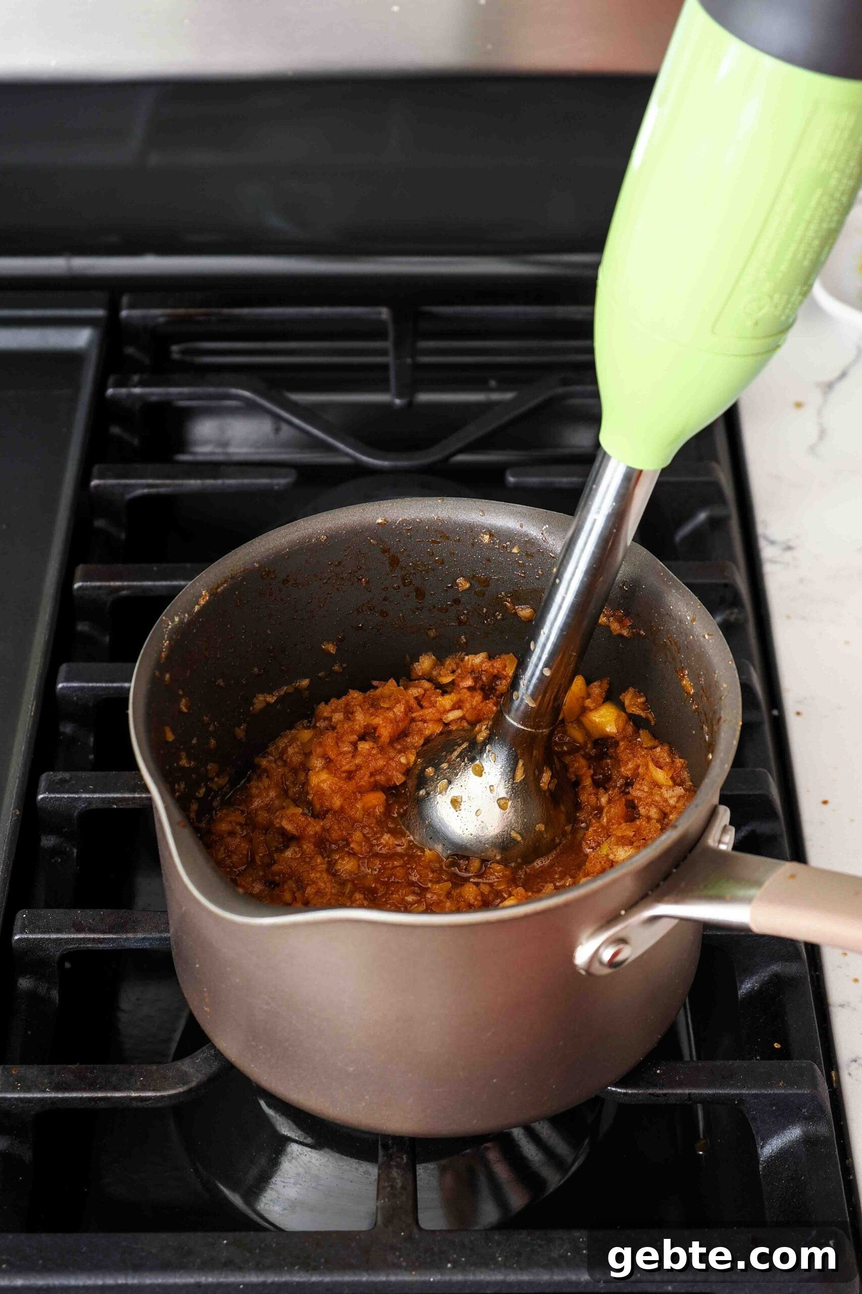An immersion blender blends together spiced apple filling in a pot.