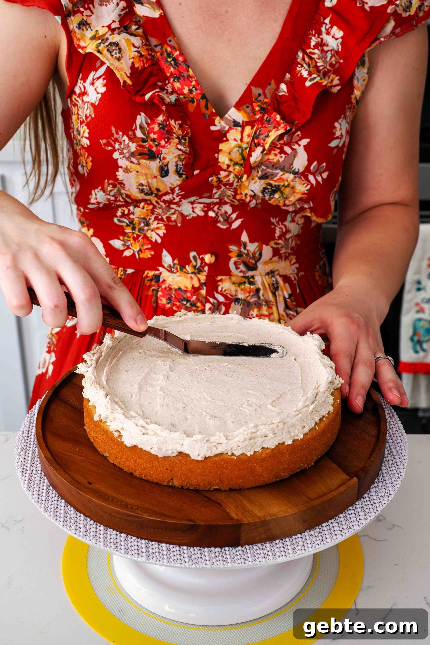 A woman smooths cinnamon buttercream on a cake layer with an offset spatula.
