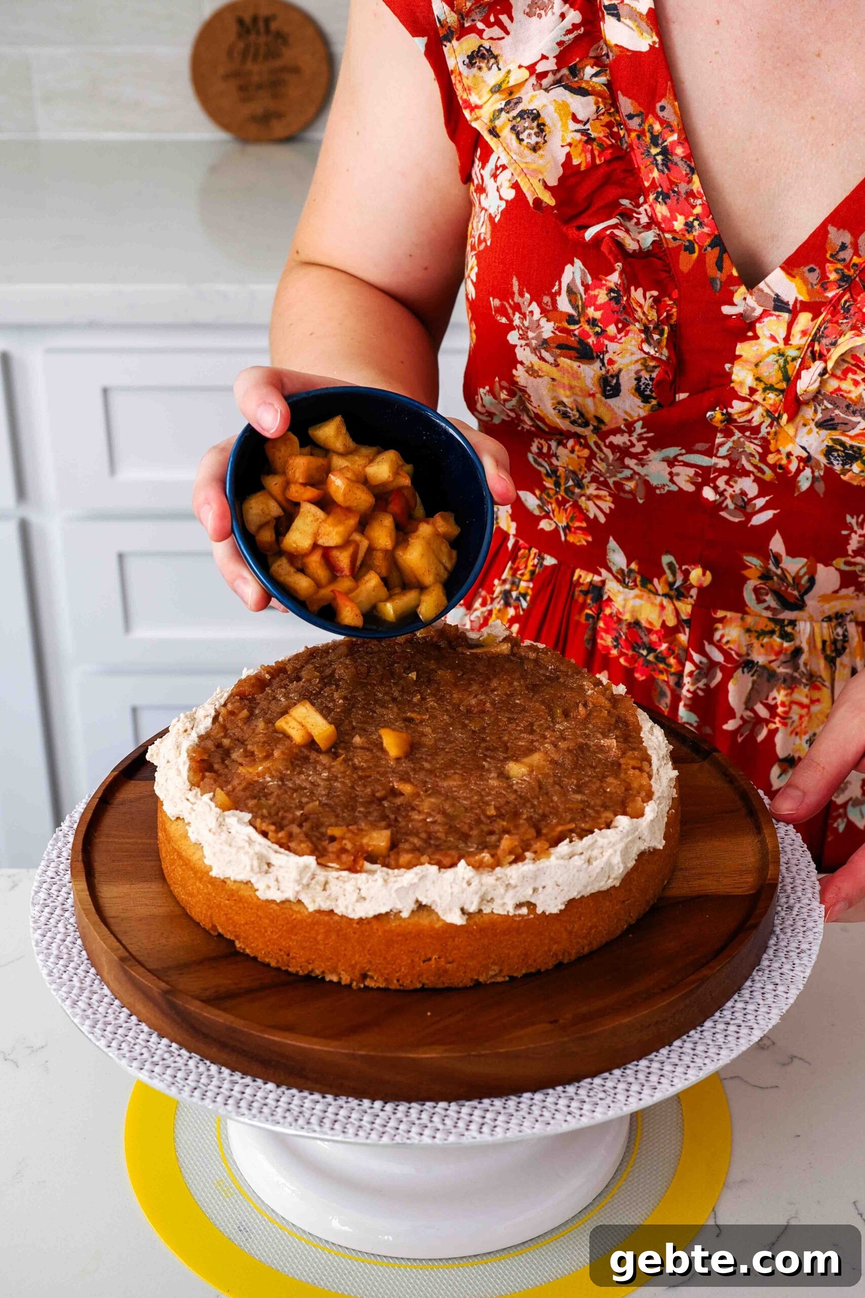 A woman sprinkles cooked apple pieces on top of a spiced apple cake filling.