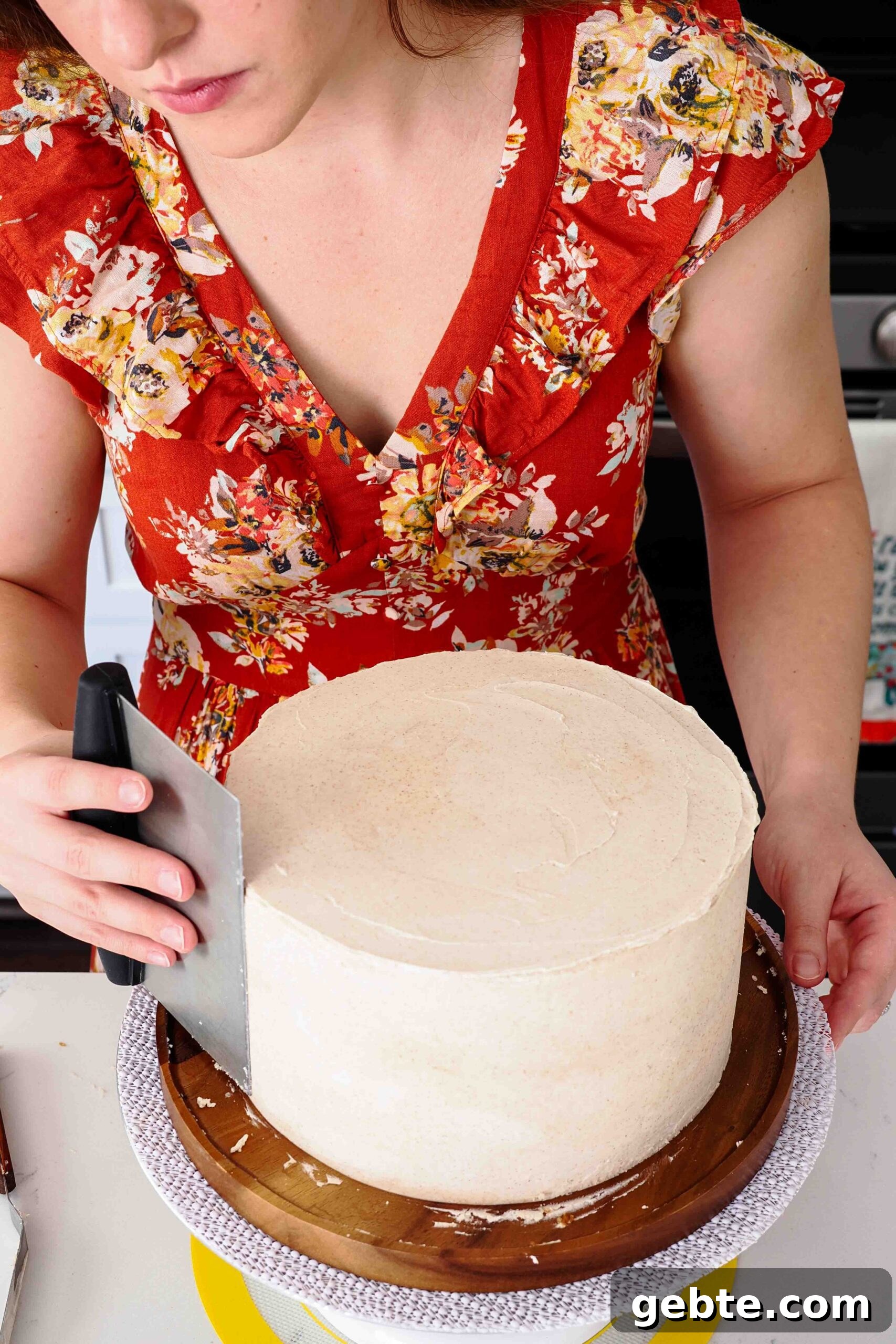 A woman smooths the sides of a cake frosted with cinnamon buttercream.