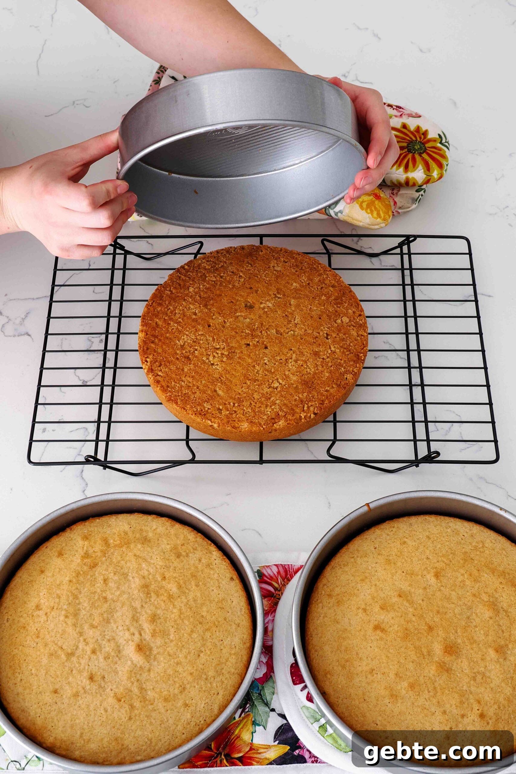 Two hands turn out an 8-inch cake from a pan.