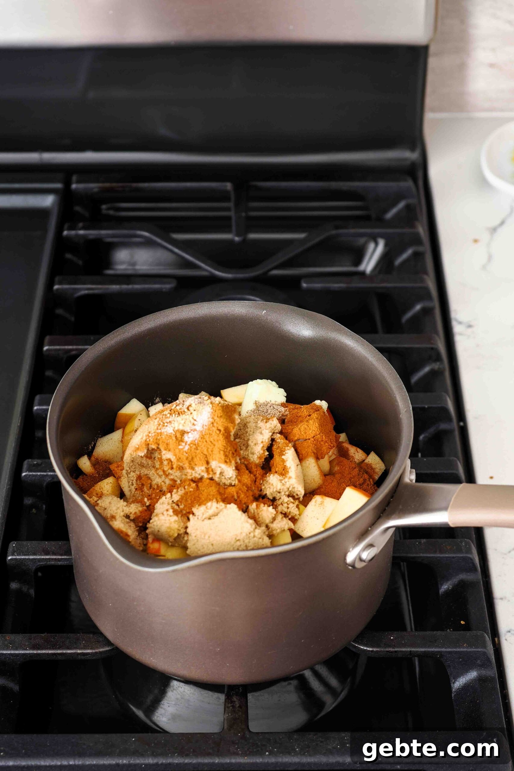Apple pieces, brown sugar, and spices in a saucepan.