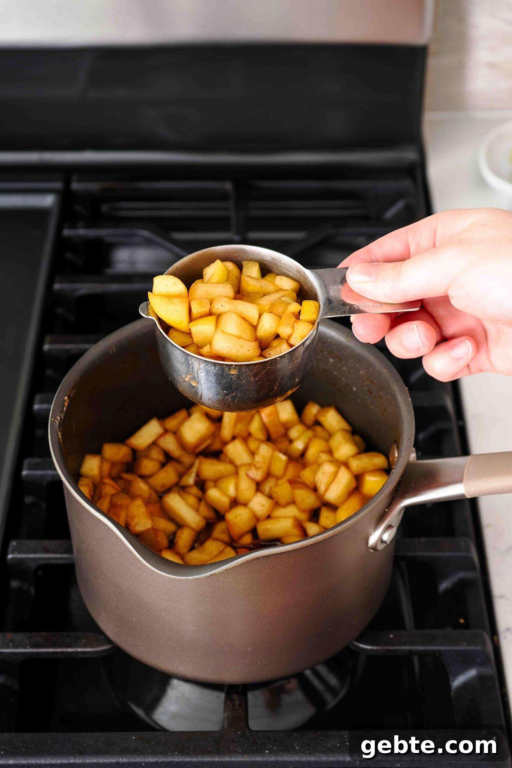 One cup of cooked and spiced apple pieces is removed from a pot.
