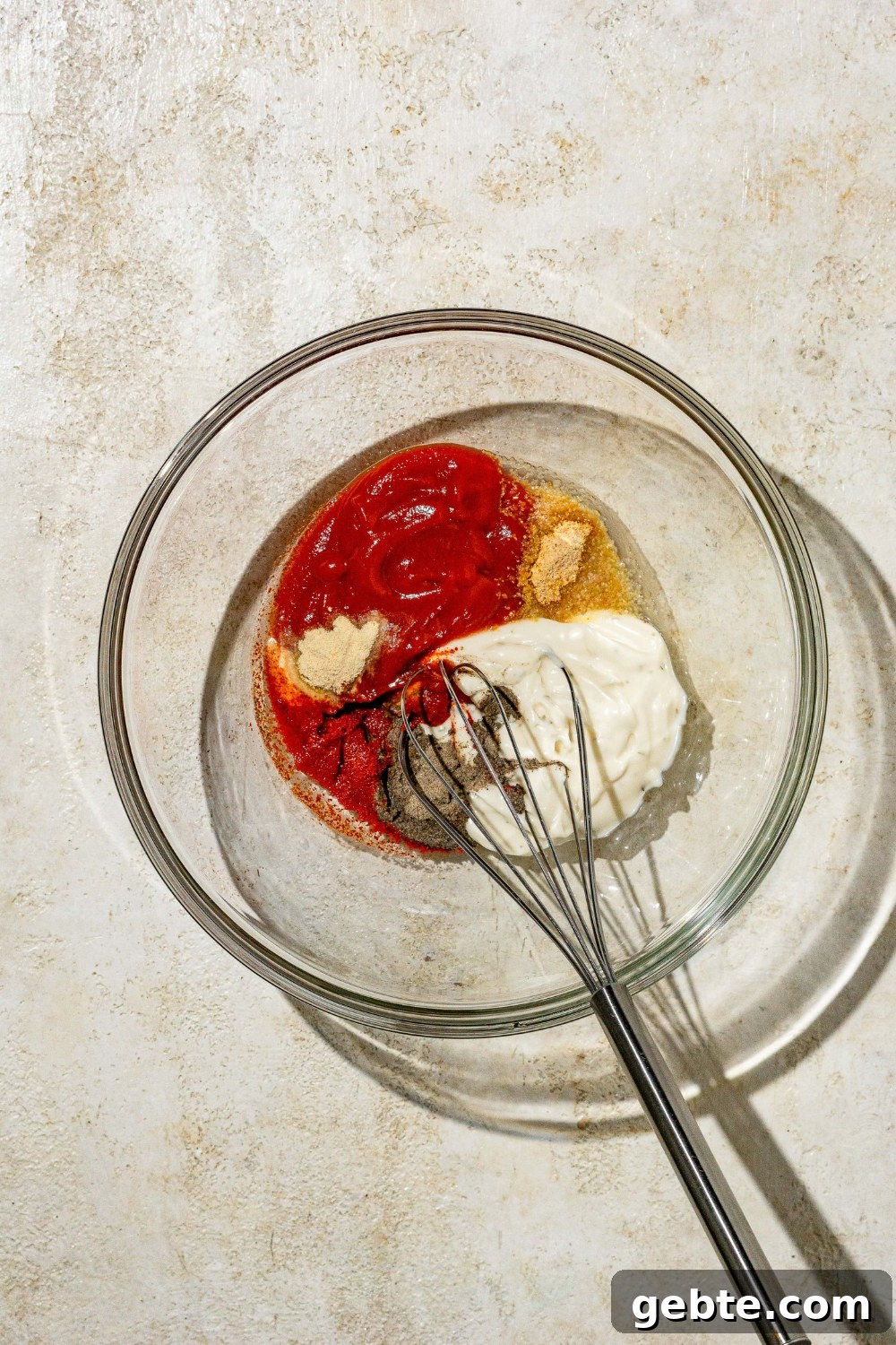 A glass bowl with a whisk mixing ingredients to make copycat Zaxby's sauce. The bowl is on a tan counter.