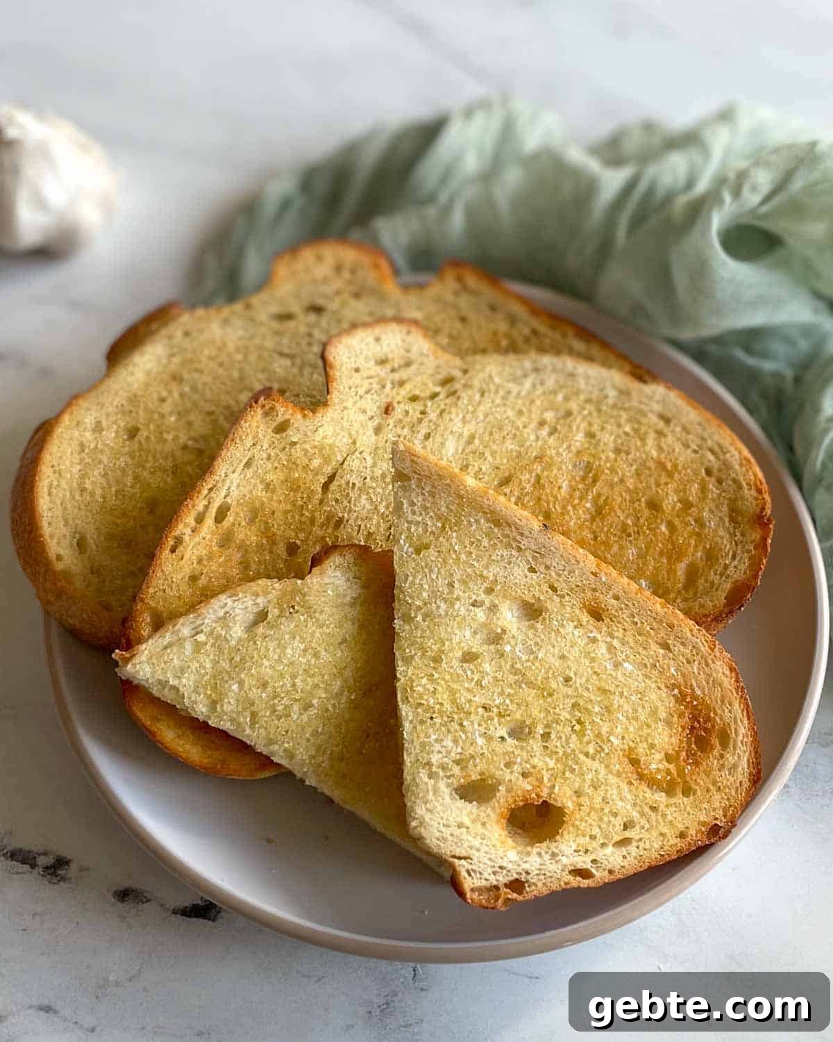 Three slices of toasted bread are shown on a white plate on a white marble counter with a light green linen.