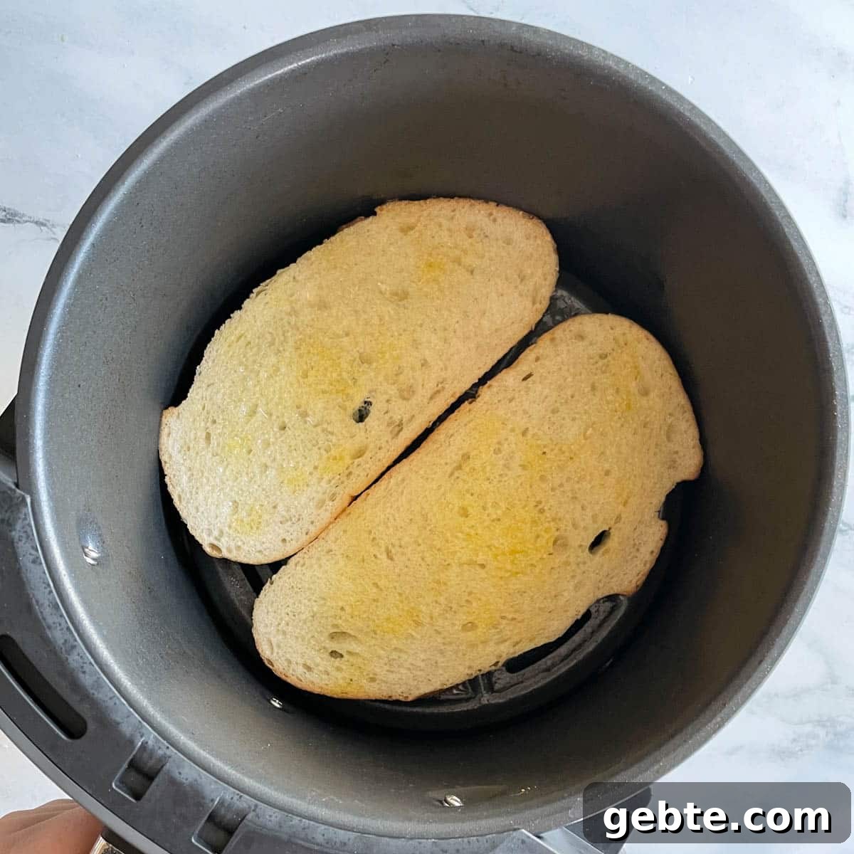 Two slices of bread brushed with olive oil are shown in the basket of an air fryer.