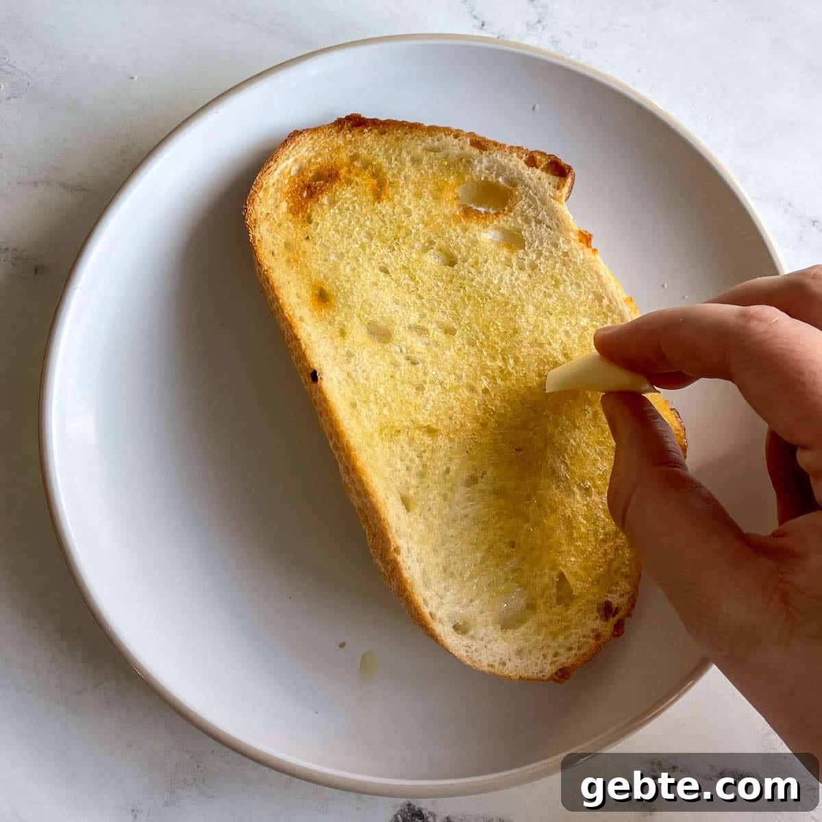 A piece of toasted bread is rubbed with a clove of garlic.