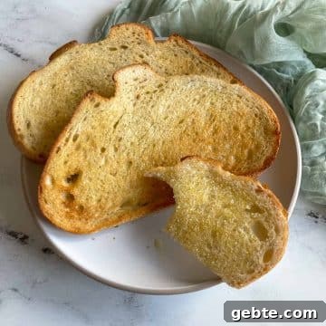 Three slices of toasted bread--one with a bite taken out of it--are shown on a white plate on a white marble counter.