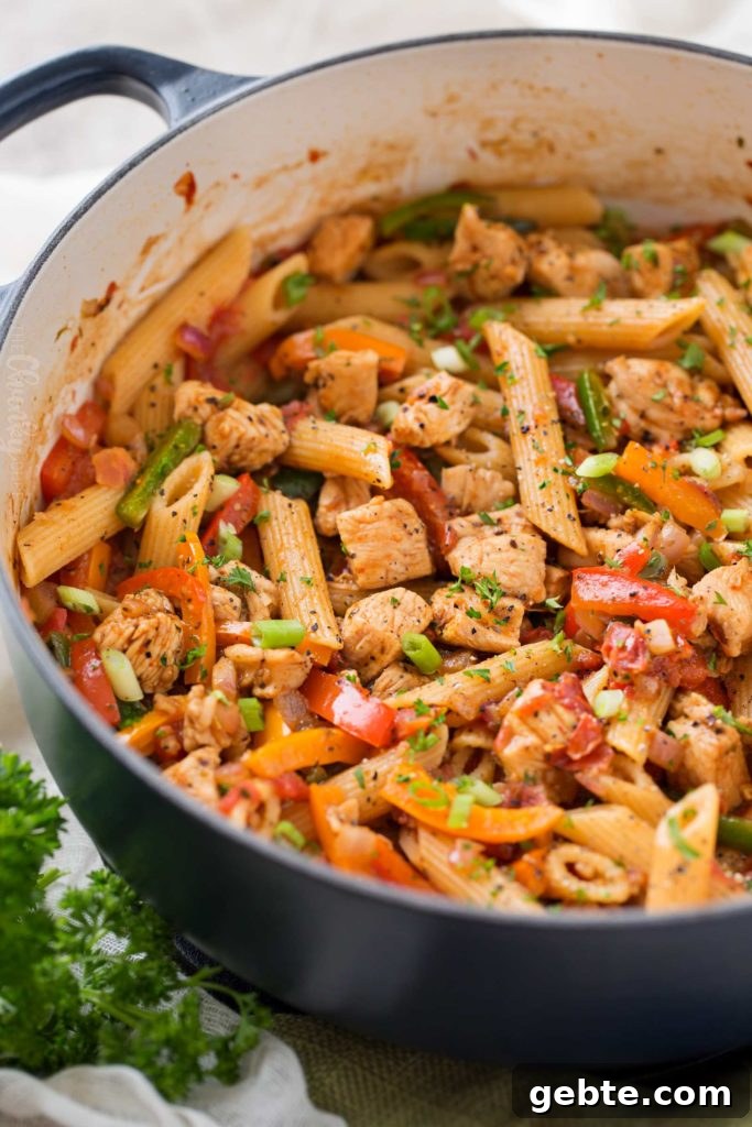 A large pot is filled with cooked penne pasta that's coated in visible spices and has diced peppers, green onions, and chicken breast.
