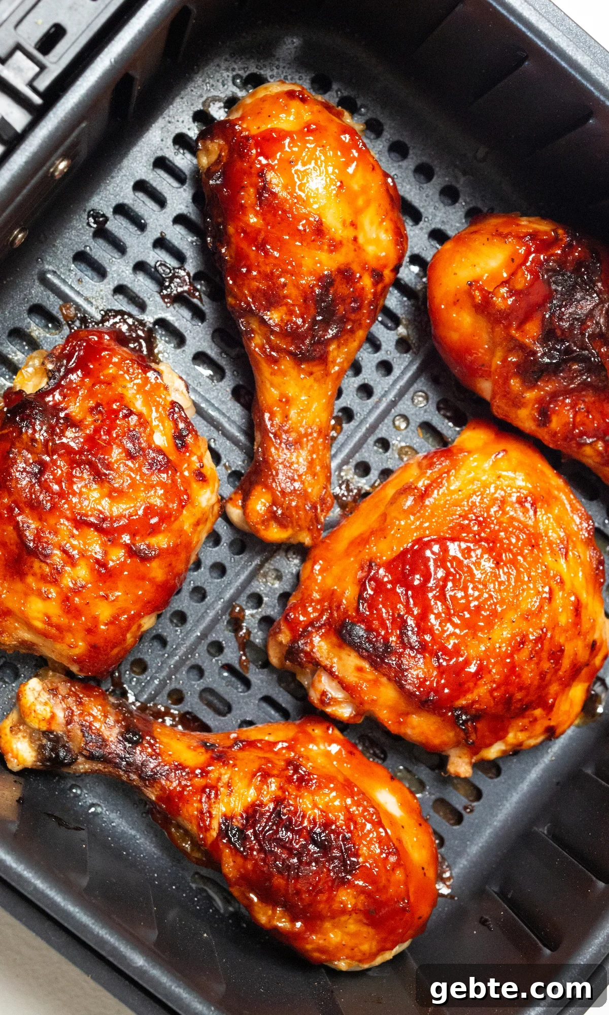 Cooked BBQ chicken legs and thighs in an air fryer basket.