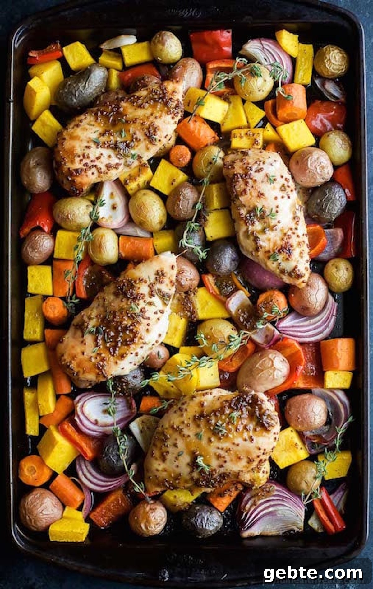 A sheet pan filled with chopped root vegetables, red onion, and seasoned chicken breasts with large sprigs of thyme.