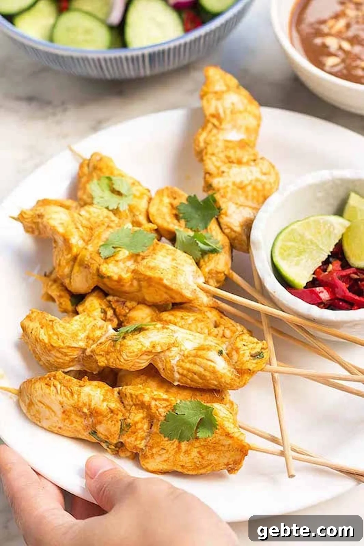 A white serving plate is filled with skewers of chicken that have been marinated in an orange sauce and then cooked. A bowl of limes and spicy peppers is on the side.