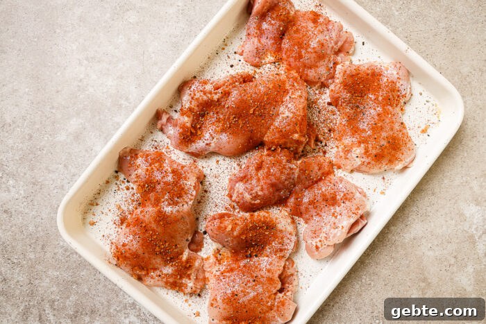 Raw, seasoned chicken thighs on a white platter.