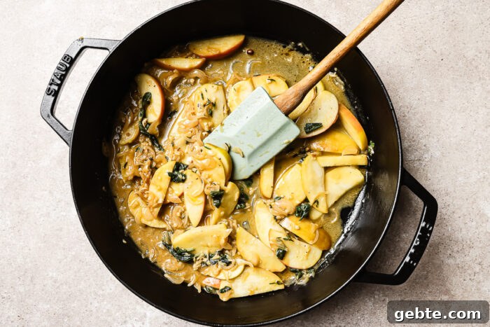 Apple cider sauce with apple slices in a cast iron skillet, reducing to a rich and flavorful glaze.