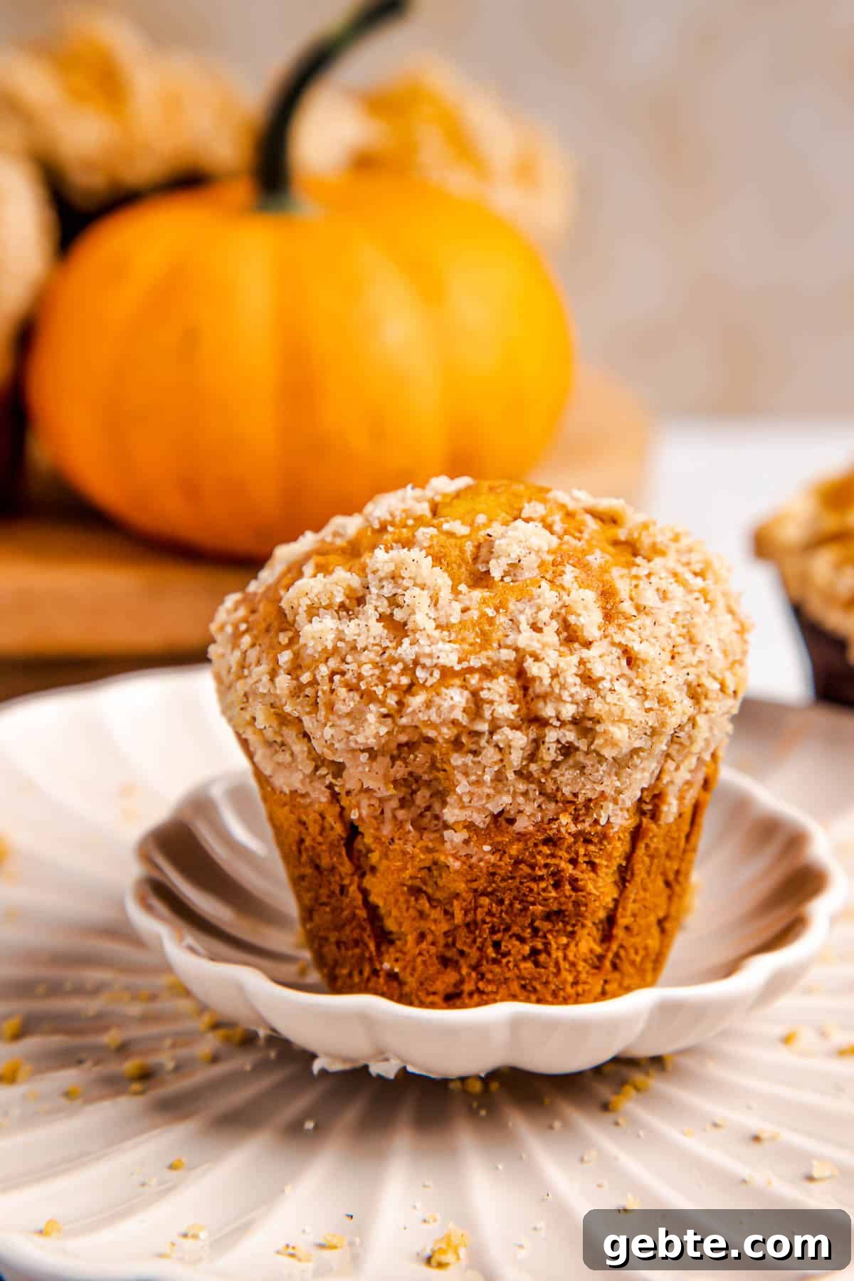 one pumpkin muffin on a white plate with three muffins behind it.