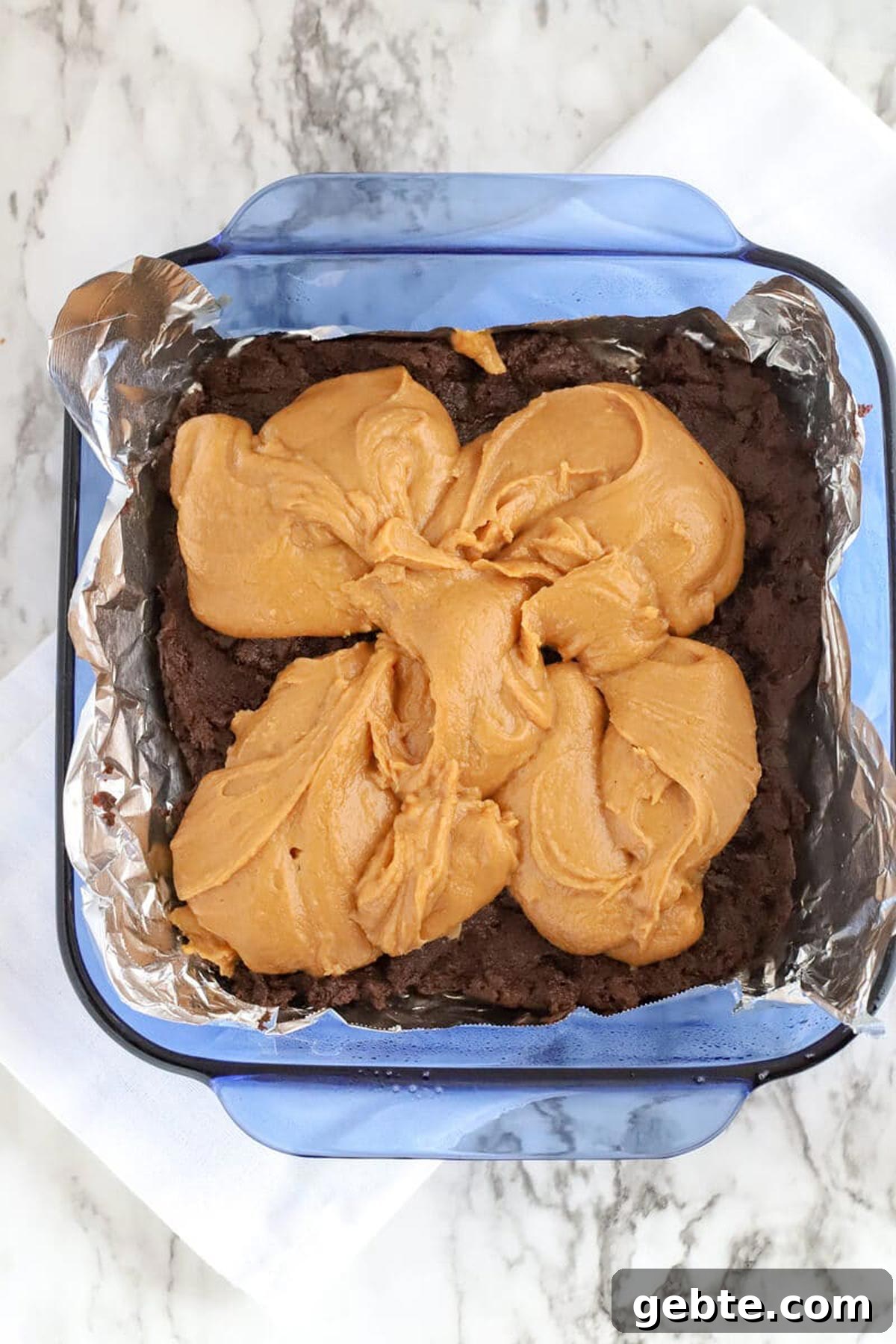 8x8 blue glass dish containing chocolate and peanut butter for making fudge.