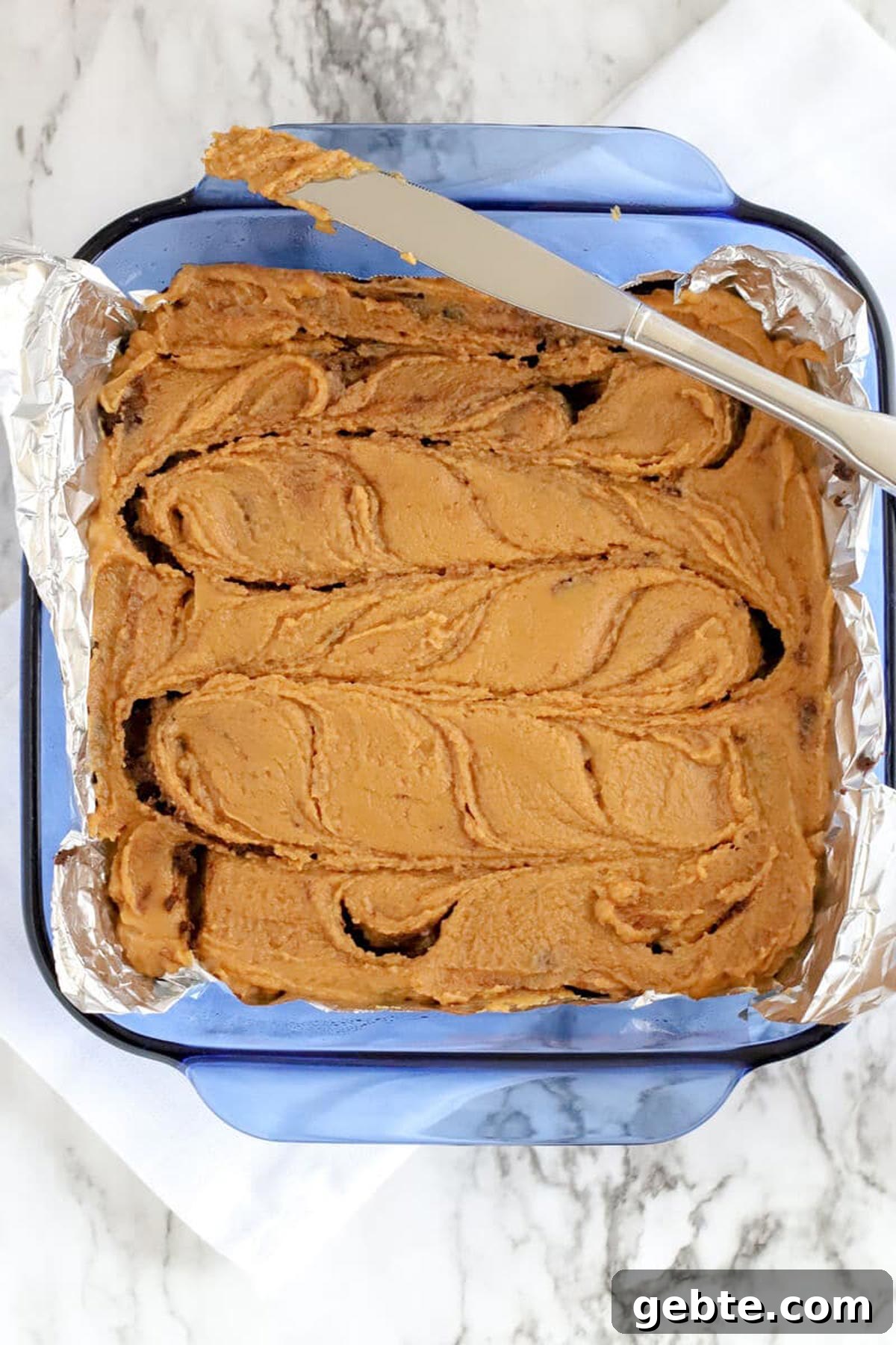 Chocolate Peanut Butter Fudge swirled with a butter knife in a blue baking dish.