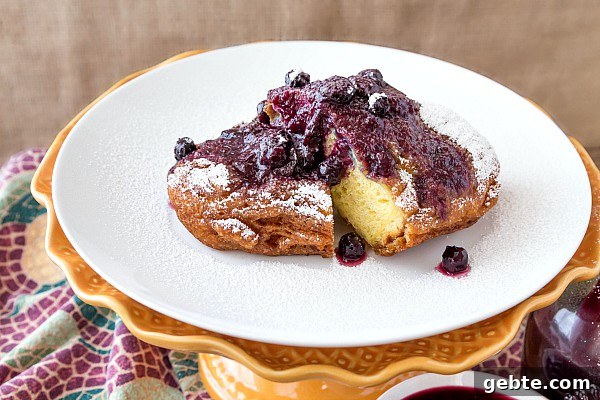 Crispy Deep Fried French Toast for Your Dream Brunch 5 Sliced french toast with whole blueberry and peach sauce and some powdered sugar on top, One slice is missing.