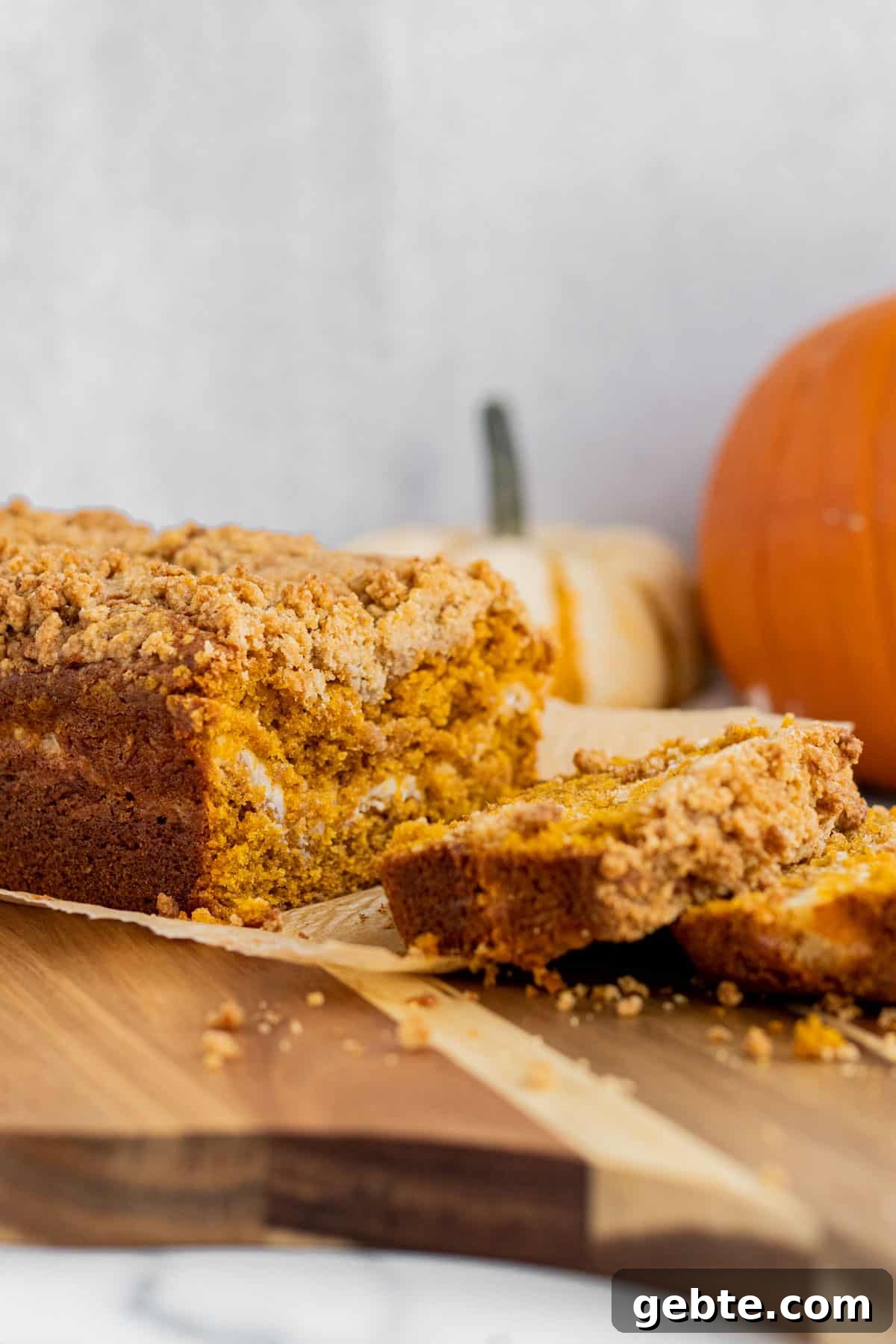 Pumpkin Cream Cheese Swirl Bread 2 loaf of pumpkin cream cheese bread sitting on a wood cutting board with 2 slices cut. 2 pumpkins in the background.