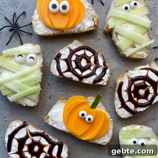 Slices of bread with cream cheese are decorated for Halloween as mummies, spiders, and pumpkins using cucumber, yellow vegetables, balsamic glaze, and candy eyes. Plastic spiders are placed around the snacks.